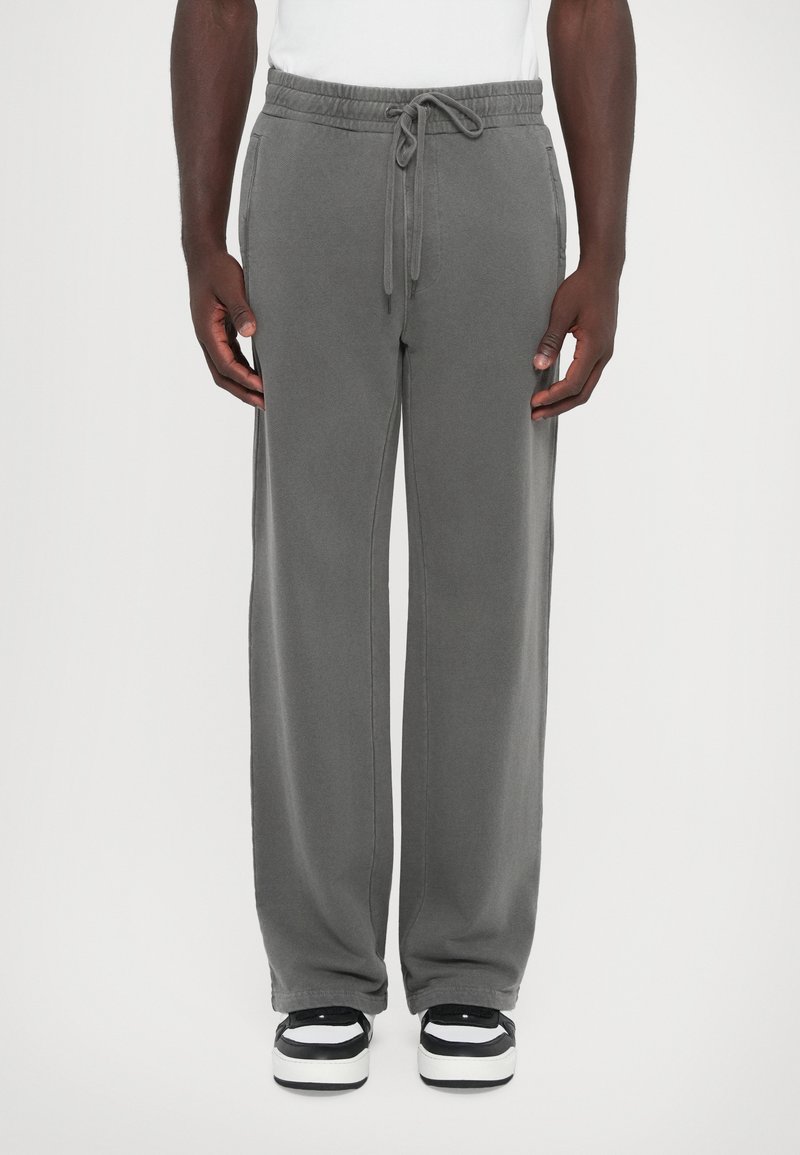 Gray sweatpants with a drawstring waist, side pockets, and a loose fit, paired with black and white sneakers. Smooth texture.