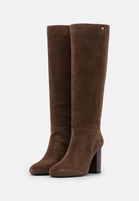 Bottines en suède marron montantes jusqu'au genou, avec un bout rond et un talon carré. Elles présentent une texture lisse et un petit logo en accent sur le côté.