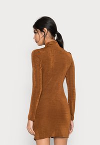 Vestido castanho justo de mangas longas com uma gola alta, tecido texturizado e bainha ligeiramente evasê, exibindo uma cor sólida e um acabamento suave.