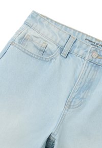 Jeans de denim azul claro con bolsillos frontales, trabillas para cinturón, cierre de botón metálico y detalle de costura visible.