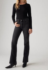 Haut noir à manches longues côtelé associé à un jean évasé taille haute en denim noir et des bottines noires à bouts pointus. Texture lisse et coupe ajustée.