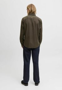 Donkergroene button-up shirt met een achterkant yoke, gecombineerd met donkerblauwe rechte jeans. Beschikt over standaard manchetten en een afgeronde zoom.