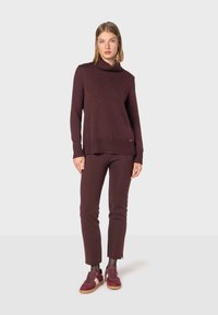 Bordeaux gestrickter Pullover mit hohem Kragen, gerippten Kanten, kombiniert mit passenden Hosen und burgunderfarbenen Sneakers mit sandfarbenen Akzenten.