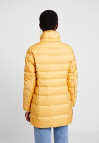Yellow quilted puffer jacket with a high collar, ribbed texture, and a loose fit. Features long sleeves and a mid-thigh length, practical design.