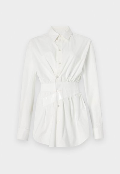 Balta marškiniai su ilgomis rankovėmis, prigludusi juosmens detalė ir blizganti diržo akcentas. Pagaminta iš lygaus, lengvo audinio.