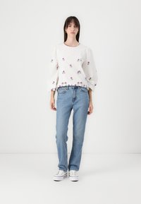 Blusa bianca a maniche a palloncino con ricami floreali, abbinata a jeans dritti azzurri e sneaker bianche. Design minimalista, tessuto morbido.