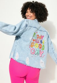Giacca in denim azzurro chiaro con effetto usurato, caratterizzata da un ricamo colorato con la scritta "OGGI SARÀ UNA BELLA GIORNATA" sulla schiena, con dettagli sfilacciati sull'orlo.