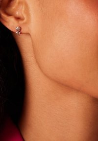 Silberne Blumenohringe mit einem kleinen runden Stecker und einem Blütenblatt-Design, vor einem Nahaufnahmebild von Haut mit gleichmäßiger Textur.