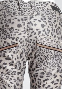 Jean imprimé léopard avec une base gris clair et des taches gris foncé. Comprend deux poches arrière avec des fermetures éclair noires et des accents métalliques.