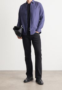 Marinblå knapp-up skjorta, svart t-shirt, svarta byxor, svarta skor, håller en svart kuvertväska; minimalistisk design med standard passform.