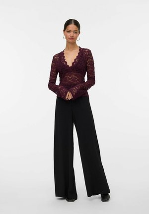 Top in pizzo bordeaux a maniche lunghe con scollatura e polsini a onda, abbinato a pantaloni neri a gamba larga e scarpe nere.