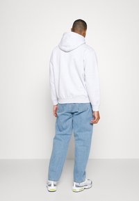 Grå hettegenser med avslappet passform, brukt sammen med lyseblå løstsittende jeans og hvite joggesko, sett fra baksiden.