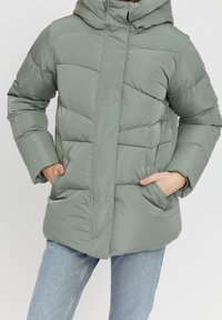 Lysgrøn oppustelig jakke med hætte, der har stikninger, to frontlommer og lynlåslukning foran. Glat, vandafvisende materiale.