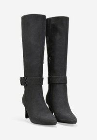 Botas negras hasta la rodilla con un acabado de ante suave, puntera afilada y una correa frontal con una hebilla de metal; cuenta con un zipper lateral para facilitar su uso.