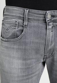 Grå denimjeans har en klassisk femficksdesign, subtil blekning och en metallknappsstängning med sömnadsdetaljer på fickorna.