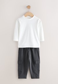 Chemise blanche à manches longues avec un col rond, associée à un pantalon cargo gris foncé doté de deux poches latérales et d'une taille à cordon.