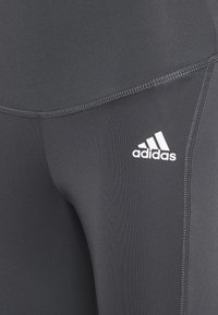 Černé sportovní legíny vyrobené z hladkého, elastického materiálu. Mají ploché švy a bílé logo Adidas na levém stehně.