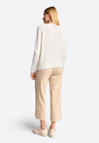 Krämfärgad tröja med en subtil textur, beige cropped byxor och ljusa sneakers. Anmärkningsvärt detalj: liten dekoration baktill.