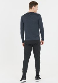 Maglietta a maniche lunghe blu navy con una texture liscia, abbinata a pantaloni sportivi neri a gamba affusolata con un sottile lucido e polsini elastici.