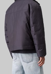 Mørkeblå jakke med en boxy design, der har ribbede kanter og krave. Glat tekstur med minimal syning, båret over lyse denim jeans.