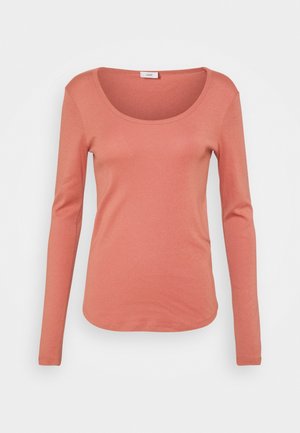 Chemise pour femme à manches longues de couleur corail rose avec encolure ronde et taille ajustée sur fond blanc.