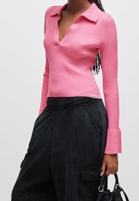 Roze geribbeld long-sleeve top met een kraag en een diepe V-hals, gecombineerd met zwarte wijde broek met een elastische tailleband.