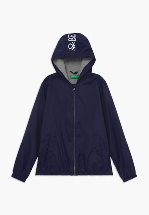 Veste à capuche bleu marine avec fermeture éclair sur le devant, poignets élastiques, deux poches latérales et texte "BENETTON" sur la capuche, doublure grise à l'intérieur de la capuche.