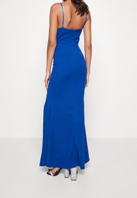 Maxiklänning i klarblått, figursydd design, tunna justerbara remmar, med en dragkedja bak och en slits på sidan, bärs med silverblockklackar.