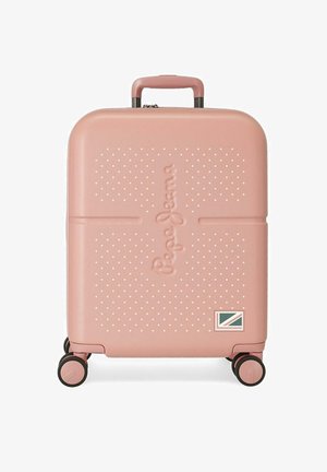 Maleta rígida compacta de color rosa con puntos texturizados, cuatro ruedas, asa retráctil y un pequeño parche con bandera en la esquina inferior derecha.