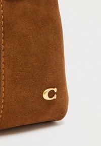 Barna szarvasbőr kézitáska arany fém logó díszítéssel és látható varrási részletekkel. Sima textúrájú, strukturált formájú.