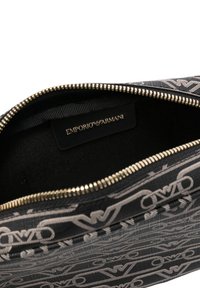 Borsa in tessuto nero con un motivo testurizzato e ripetuto del logo in grigio. Chiusura con zip dorata e etichetta interna con marchio.