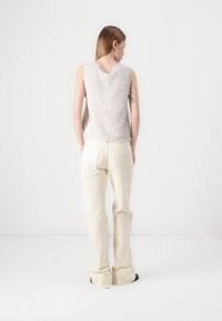 Top sin mangas de un gris claro con un acabado texturizado y un escote en V, combinado con pantalones de pierna ancha en color crema que cuentan con bolsillos traseros.