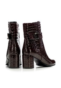 Burgundské kotníkové boty s lesklým krokodýlím vzorem. Mají přezkový pásek a blokový podpatek. Hladký povrch a design s kulatou špičkou.