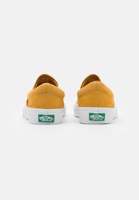 Scarpe slip-on gialle in tela con suole in gomma bianca. Presentano un sottile motivo a scacchi e il logo verde "Vans Off the Wall" sul tallone.
