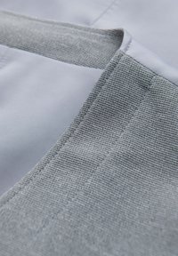 Gros plan d’un tissu gris à tissage serré avec des coutures précises sur un bord plié, montrant la texture et les détails de couture.
