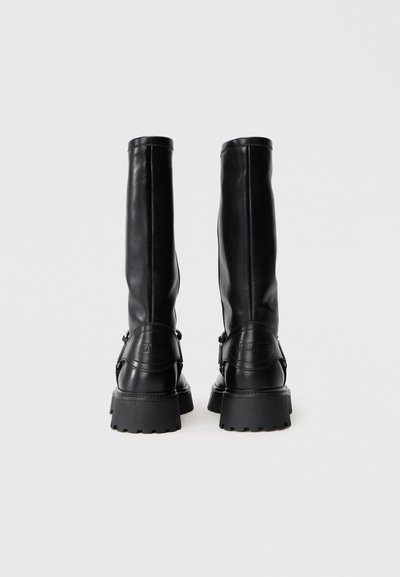 Schwarze Leder-Stiefel bis zum Knie mit flacher Sohle, runder Zehenform und seitlichem Schnallen-Detail. Glatte Textur und minimalistisches Design.