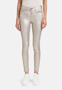 Jean skinny doré métallique avec une texture lisse, doté de cinq poches, d'une fermeture à bouton à l'avant et de baskets blanches assorties.