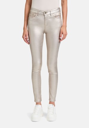 Metallic gold enge Jeans mit glatter Textur, ausgestattet mit fünf Taschen, einem Knopfverschluss vorne und passenden weißen Sneakers.