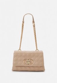 Sac à main beige matelassé avec une bandoulière chaîne en or et un fermoir doré orné d'un motif ovale. Texture douce et forme structurée.