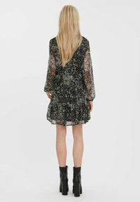 Robe noire à motifs floraux avec manches longues en voile, ourlet à volants et taille froncée. Portée avec des bottines noires épaisses. Vue de dos présentée.