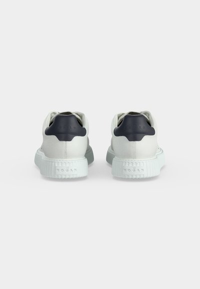 Baskets blanches avec languettes de talon noires, semelles blanches épaisses texturées, et nom de la marque embossé à l'arrière de la semelle et de la languette de talon.