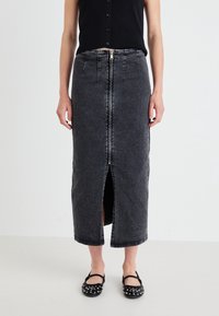 Svart denimmaxikjol med en framslits, dragkedjestängning och synliga sömmar. Kombinerad med svarta platta skor med nitar.