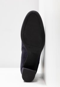 Chaussure habillée à semelle noire avec un talon carré, photographiée par le dessous, montrant la semelle et les marquages de taille.
