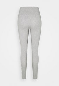 Ljusgrå högmidjade leggings visade från ryggen med en figurnära silhuett och vit text delvis synlig på nedre högra benet.
