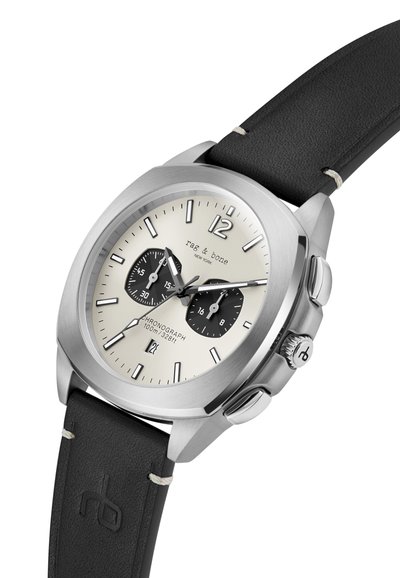 Sudraba nerūsējošā tērauda hronogrāfs pulkstenis ar melnu ādas siksnu, krēmkrāsas ciparnīcu, melniem subcipariem un arābu cipariem; ūdensizturīgs līdz 100 m.