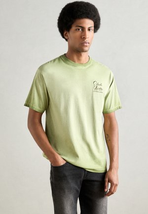 Lysegrøn T-shirt med korte ærmer lavet af blødt bomuld. Har en rundivering og et lille trykt logo på venstre bryst. Casual pasform.