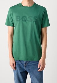 Vihreä puuvillapaita, jossa on rohkea tumma vihreä "BOSS" -kirjotus rinnassa. Lyhythihaisessa ja pyöreässä kauluksessa.