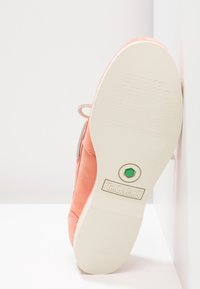 Sula av korallfärgade Timberland-skor med off-white gummisula och grönt hexagonalt detalj, placerad mot vit bakgrund.