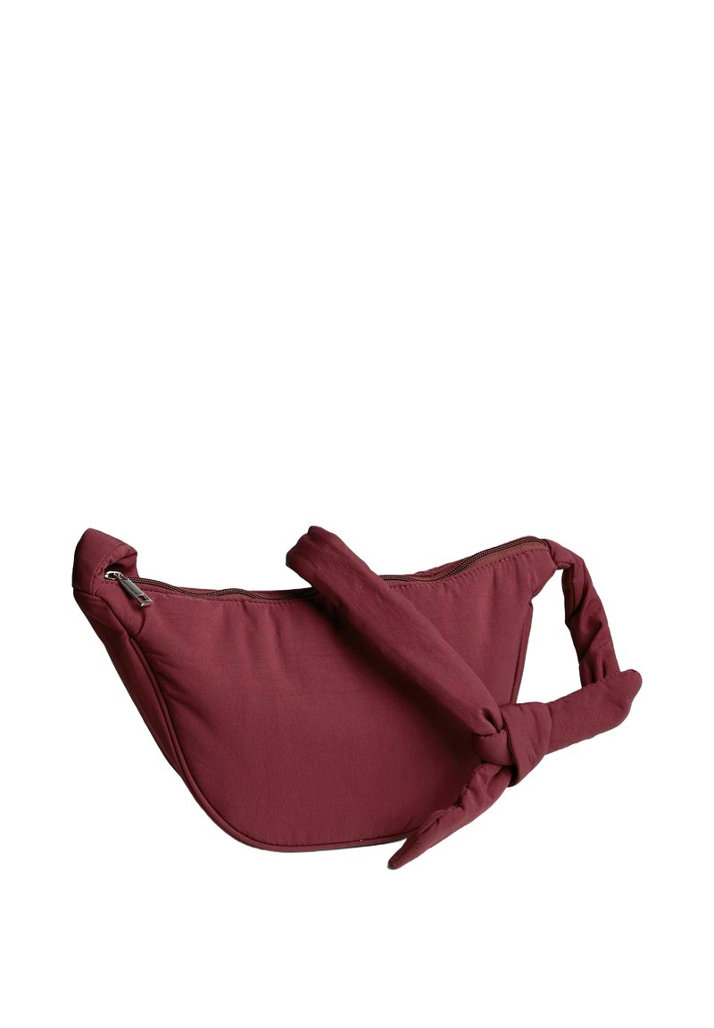 Borsa a tracolla in tessuto bordeaux con tracolla regolabile annodata e chiusura con zip superiore su sfondo bianco.