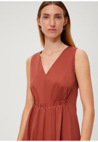 Roestrode mouwloze jurk met een V-halslijn, een gecollecteerde taille en een gladde stofstructuur. Eenvoudig, elegant ontwerp met minimale details.